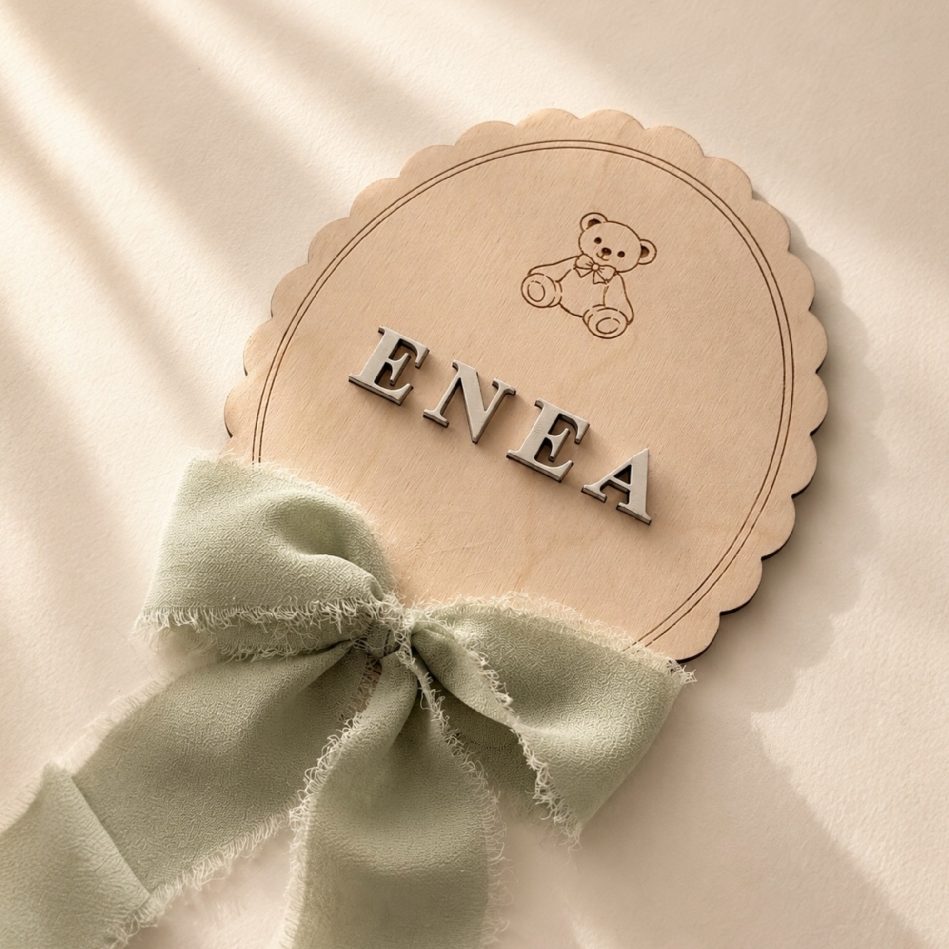 Dettaglio della targhetta nascita Teddy personalizzata in legno con nome Enea in rilievo 3D e fiocco salvia