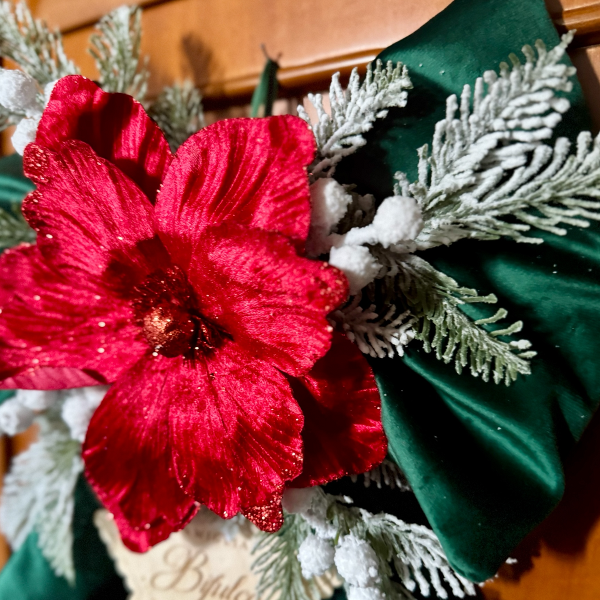 rimo piano del fiocco natalizio in velluto verde con grande fiore rosso, rami di abete innevati e bacche decorative bianche.