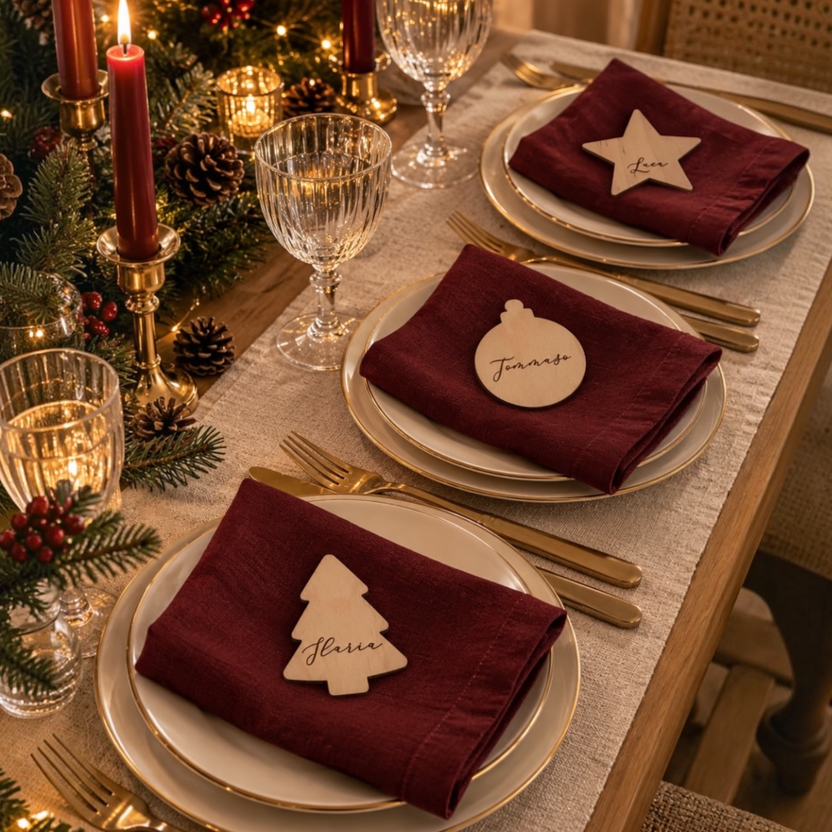 Set di tre segnaposti natalizi personalizzati in legno di betulla, a forma di albero, pallina e stella, su una tavola di Natale elegante.