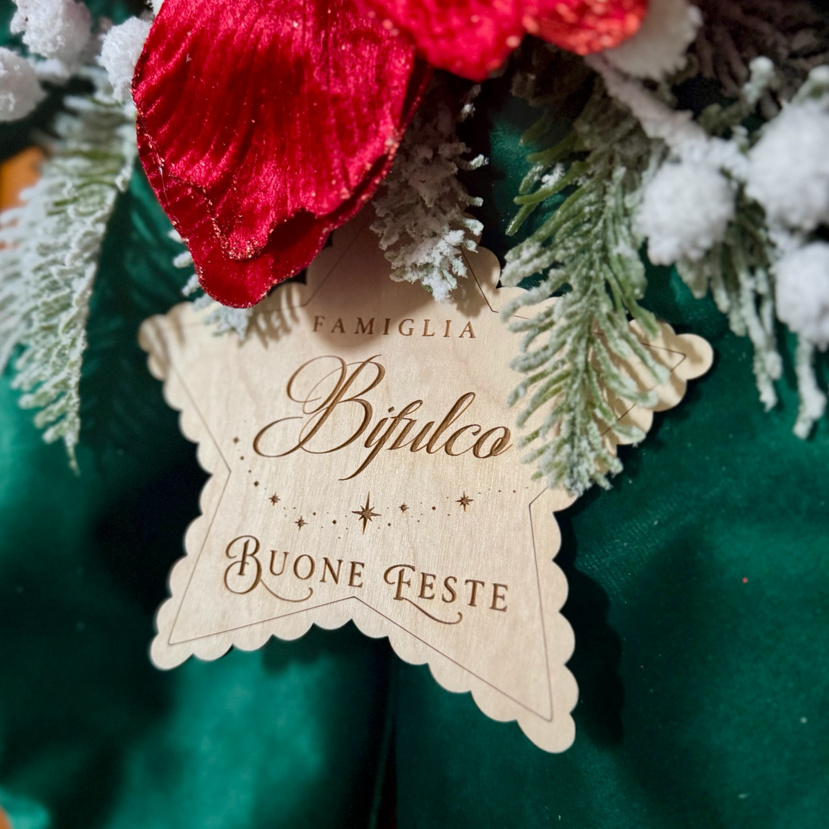Dettaglio della targhetta a forma di stella in legno con cognome personalizzato e scritta Buone Feste, sul fiocco verde.